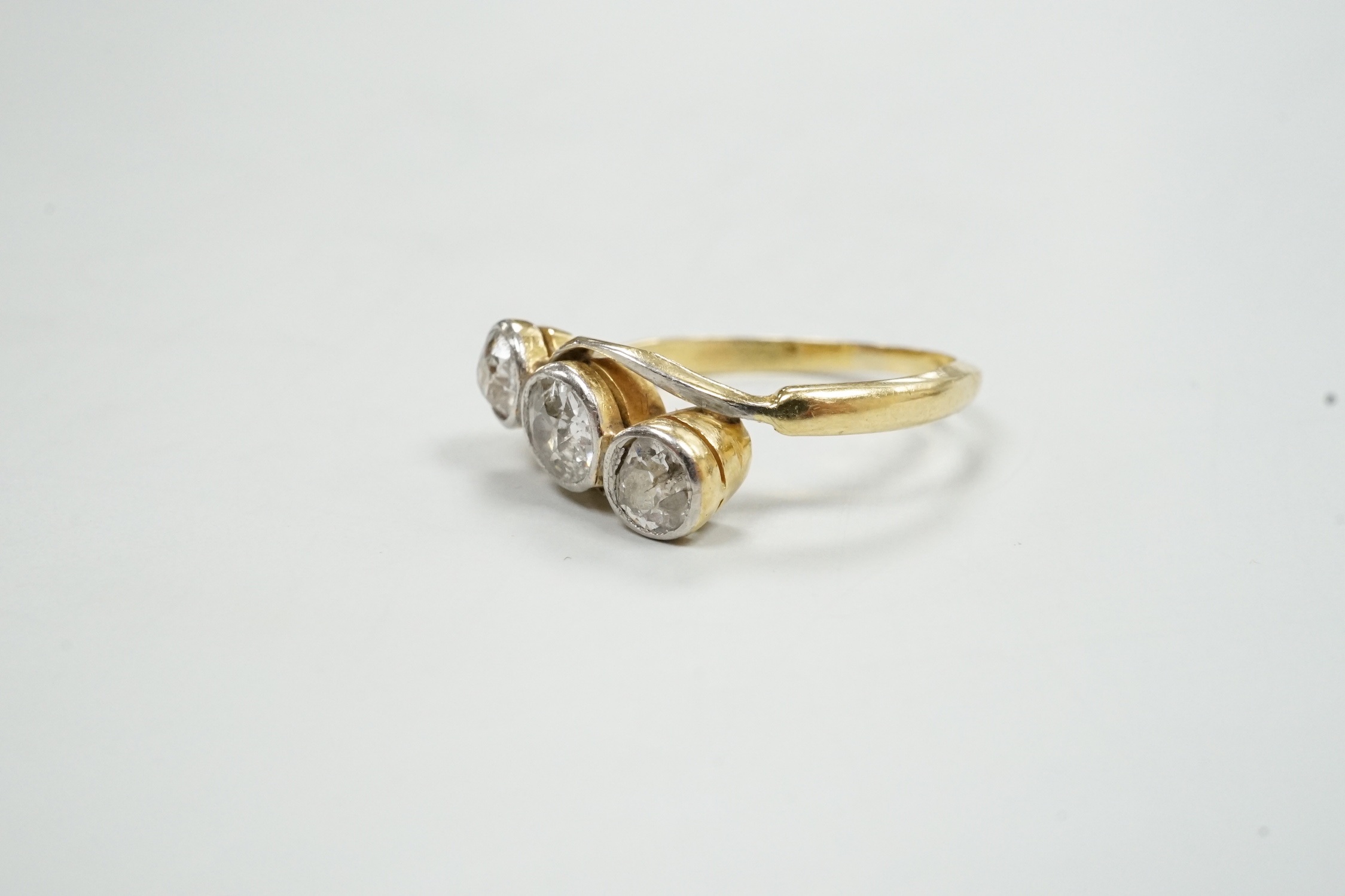A yellow metal and collet set three stone diamond crossover ring, size N/O, gross weight 3 grams.